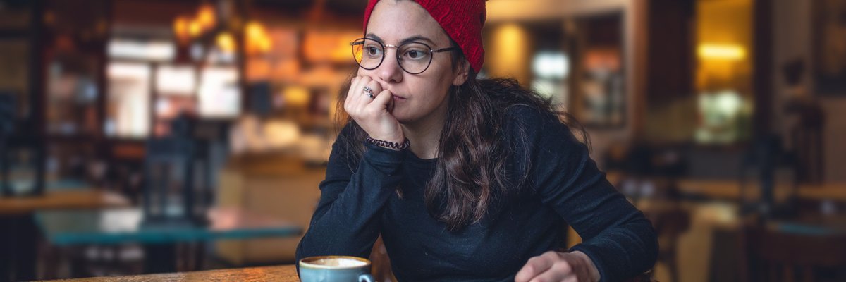 A stressed woman sitting in a cafe with her chin resting in her hand.