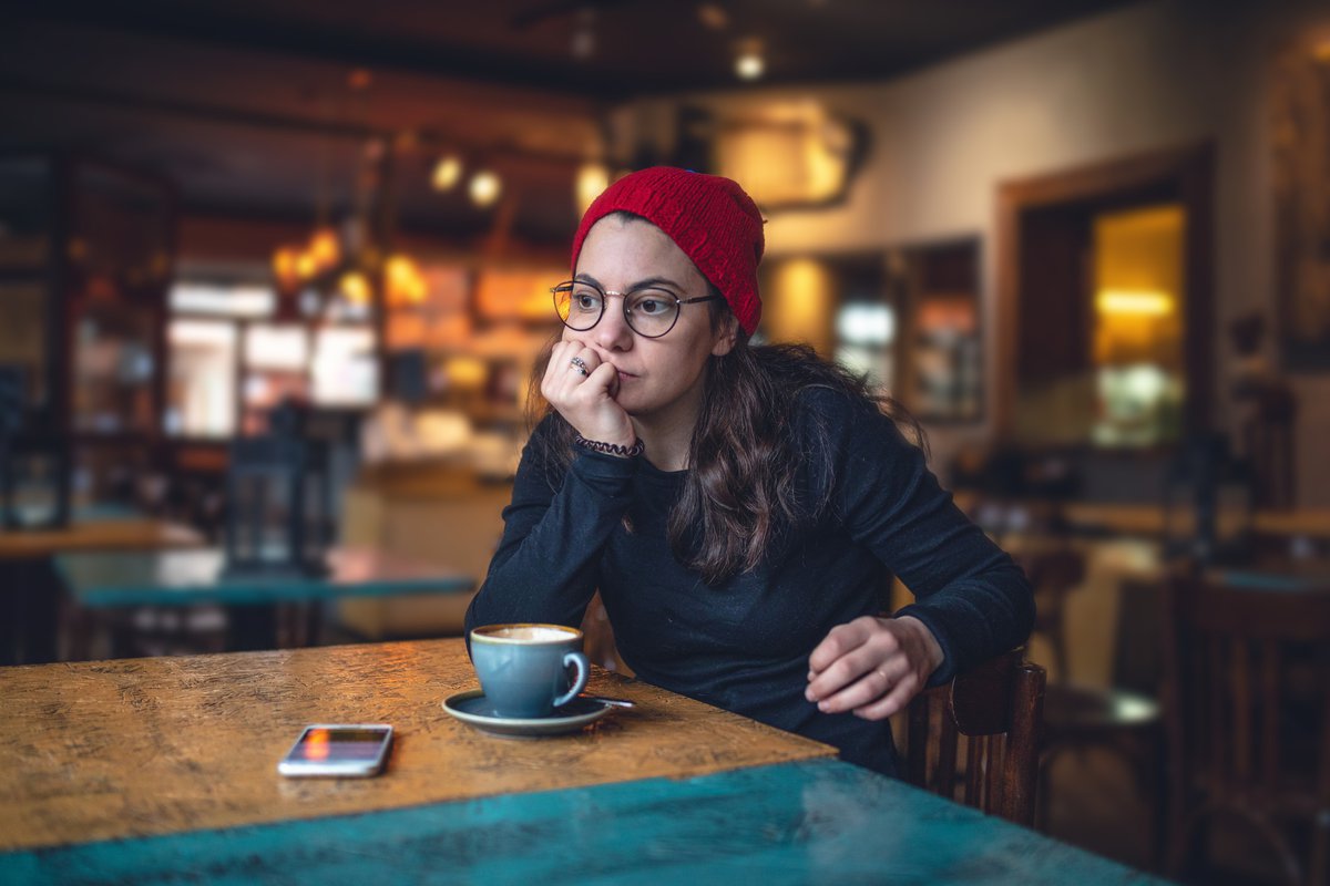 A stressed woman sitting in a cafe with her chin resting in her hand.