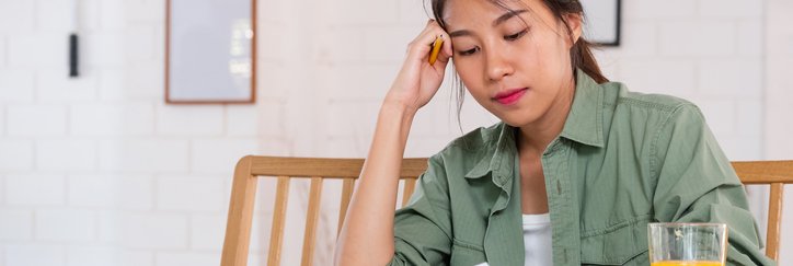 A stressed woman sitting at her dining table and looking through her bills and receipts with her head resting in her hand.