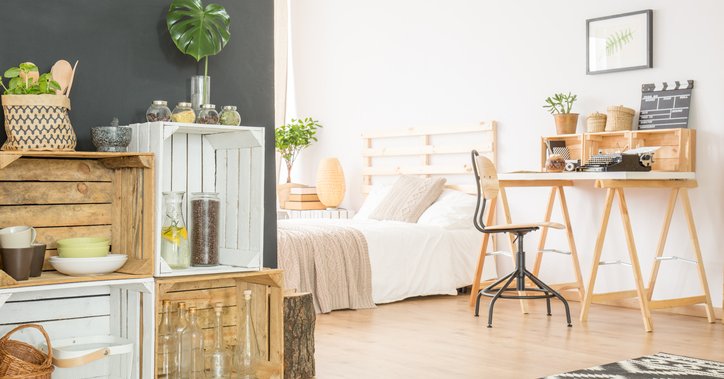 A sunny studio apartment with a desk, low bed, and wooden crates for shelves,
