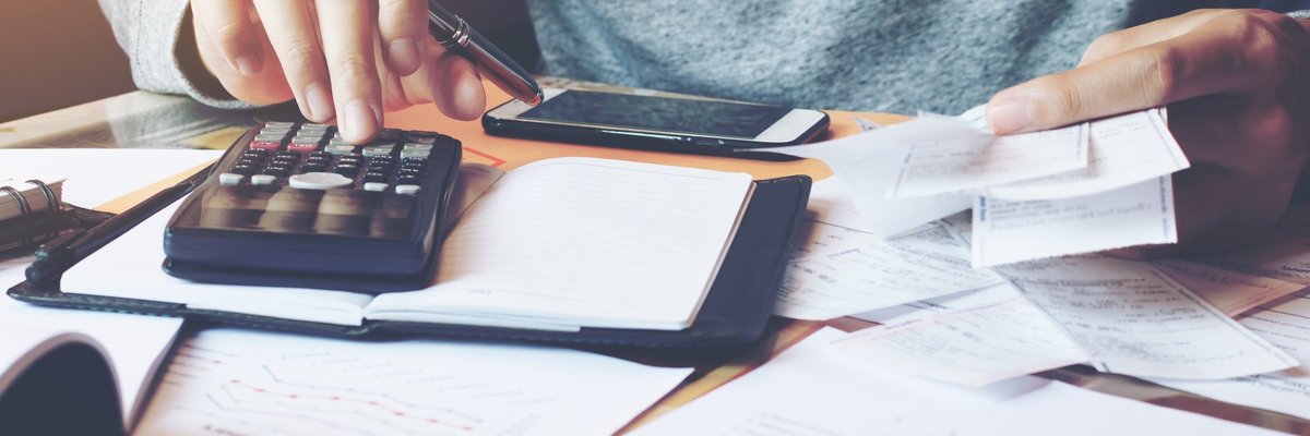 Person typing on calculator with papers spread out on table.
