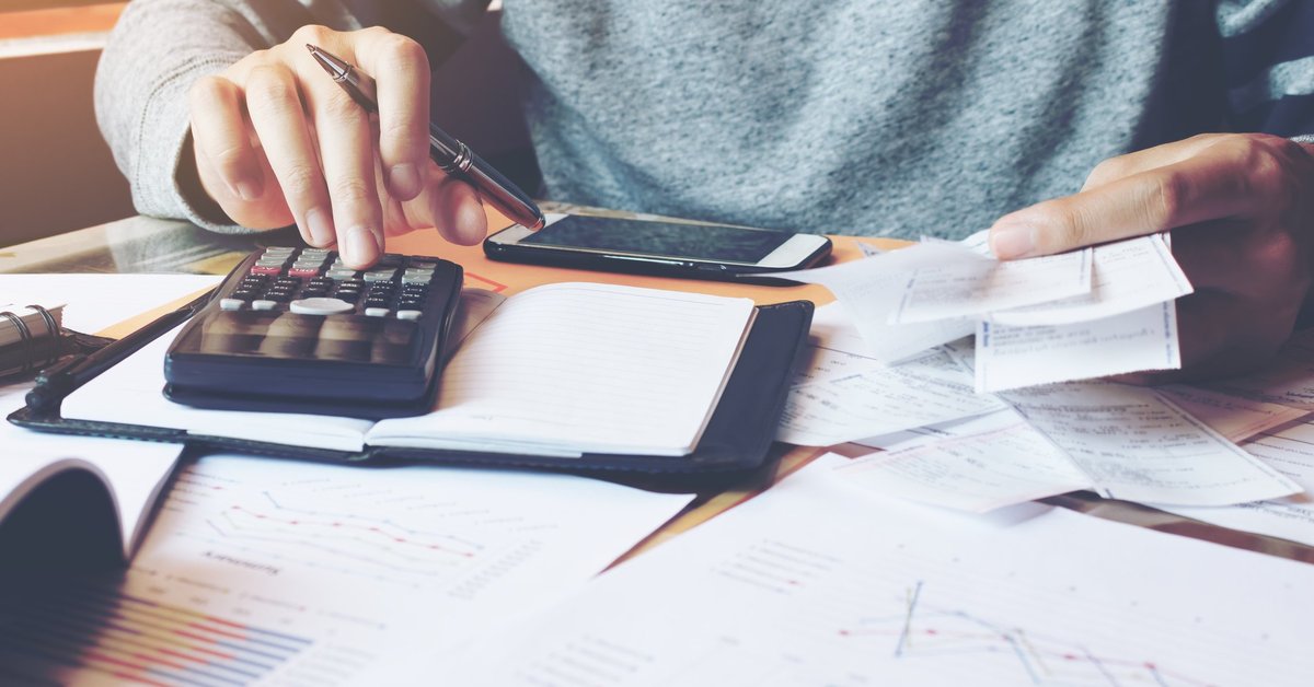 Person typing on calculator with papers spread out on table.