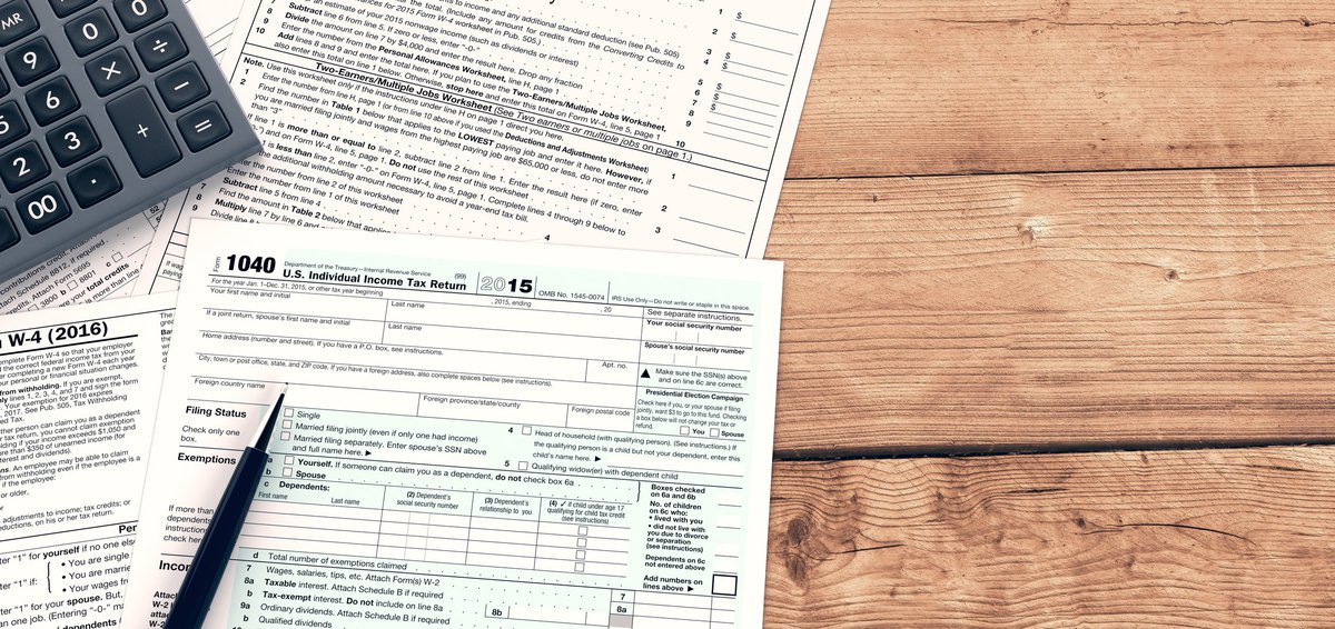 Tax forms with calculator and pen on wooden surface.