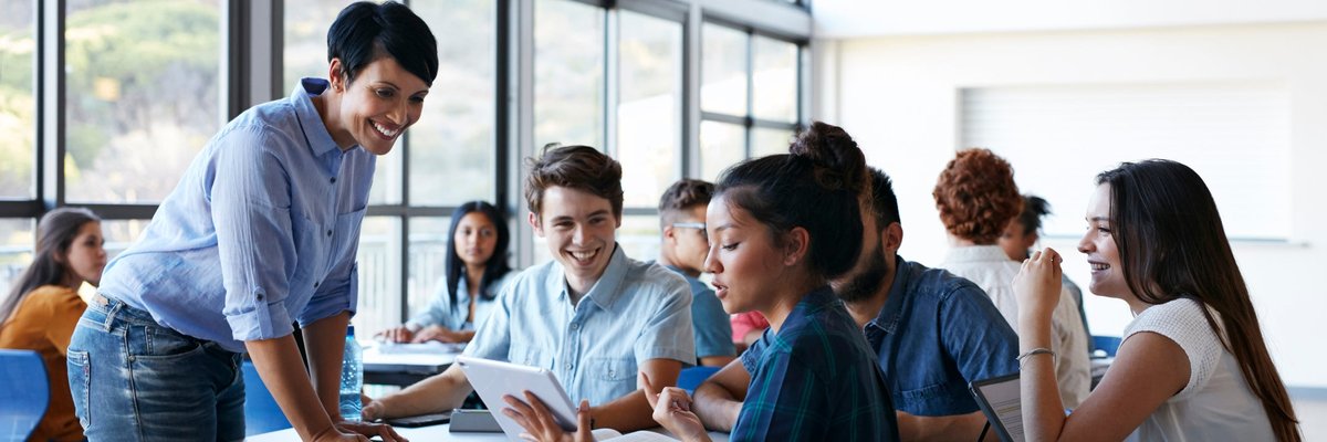 A teacher speaking with a table of students in the lunch room at a school.