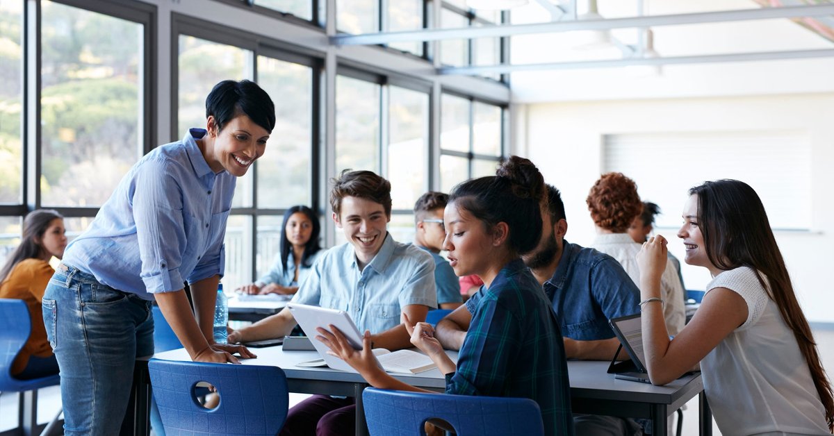 A teacher speaking with a table of students in the lunch room at a school.