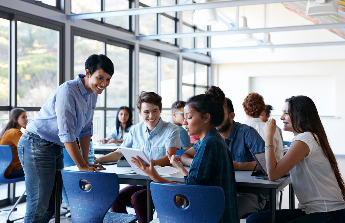 A teacher speaking with a table of students in the lunch room at a school.