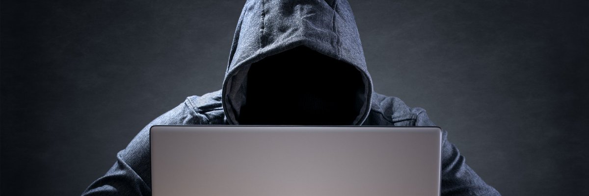 A cyber criminal wearing a hoodie and using a laptop.