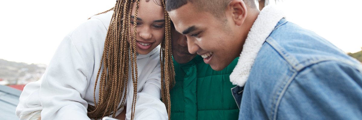 Three young people looking at a phone that one of them was holding.