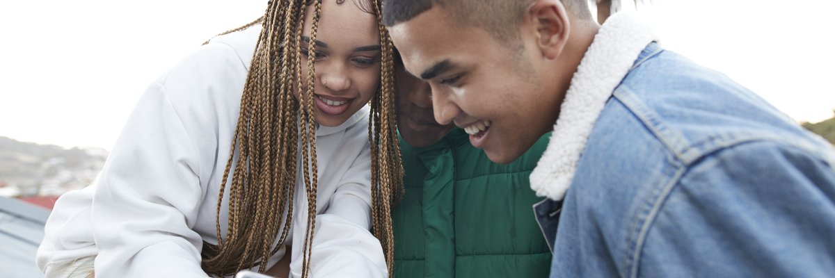 Three young people looking at a phone that one of them was holding.