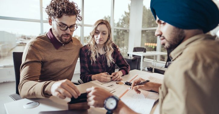 A man and woman meeting with a financial professional at his desk in an office.
