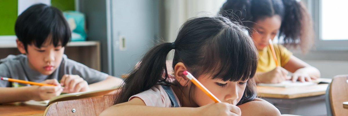 Three children sitting at desks and doing work in a classroom.