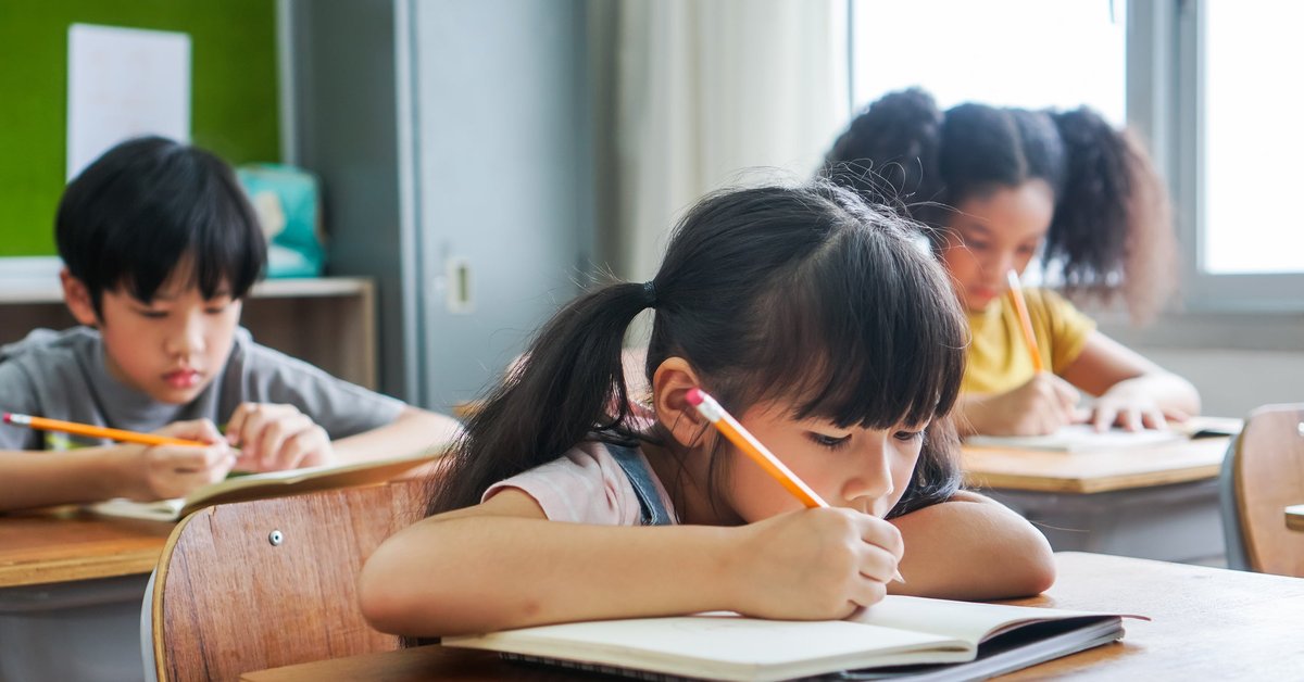 Three children sitting at desks and doing work in a classroom.