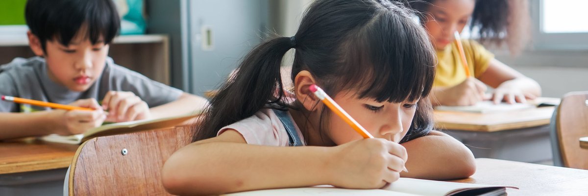 Three children sitting at desks and doing work in a classroom.