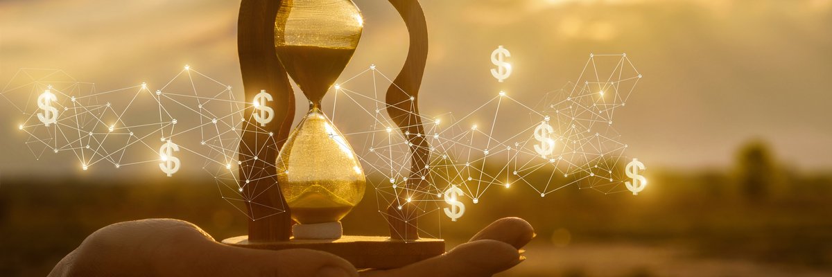 An hourglass being held in a hand outdoors.