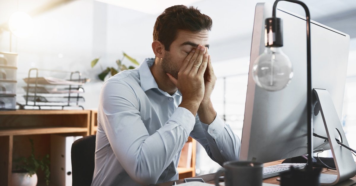A tired man rubbing his eyes and sitting at his desk at work.