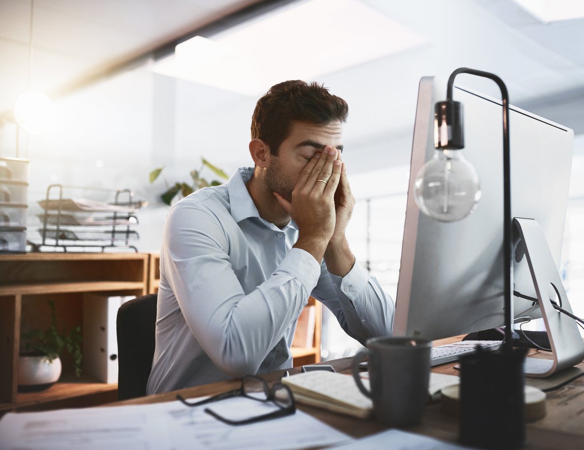 A tired man rubbing his eyes and sitting at his desk at work.