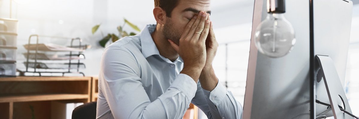 A tired man rubbing his eyes and sitting at his desk at work.