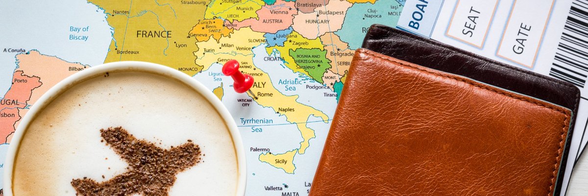 Cup of coffee with plane image in it sitting on top of map and next to a boarding pass.