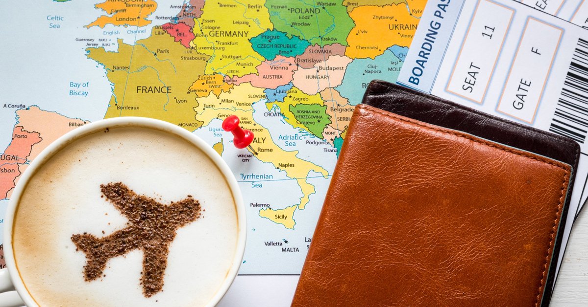 Cup of coffee with plane image in it sitting on top of map and next to a boarding pass.