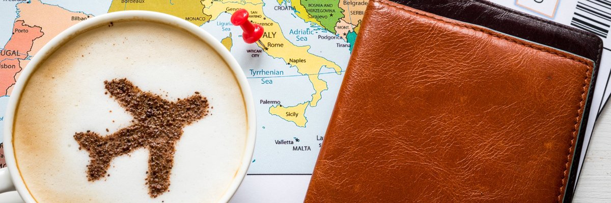 A coffee cup with a plane in the milk sitting on top of a map and next to airline tickets