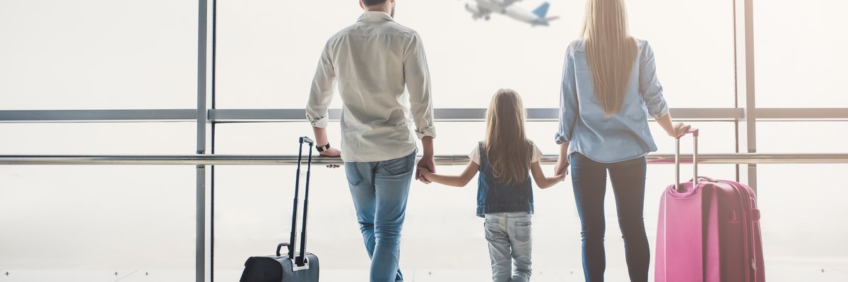 man, woman, and girl holding hands and watching airplane take off