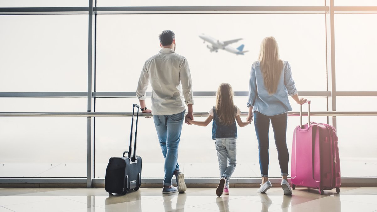 man, woman, and girl holding hands and watching airplane take off