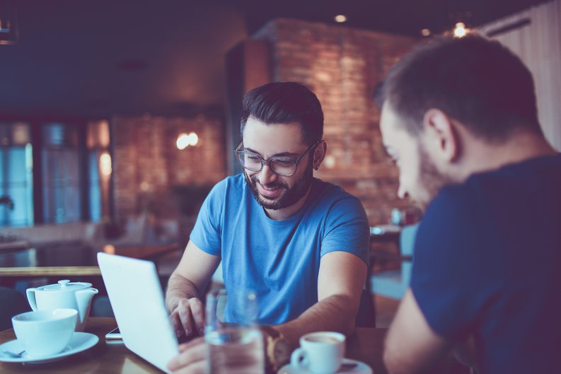 Two men looking at a laptop together in a cafe.