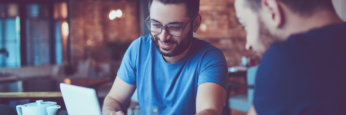 Two men looking at a laptop together in a cafe.