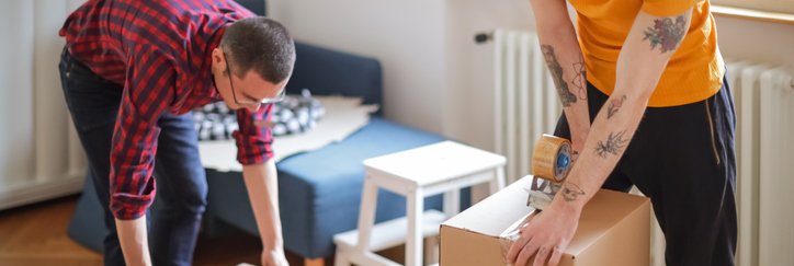 Two men taping boxes shut after packing up their living room.