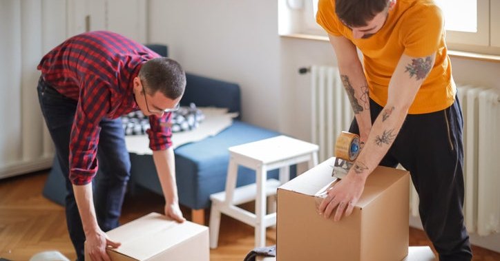 Two men taping boxes shut after packing up their living room.