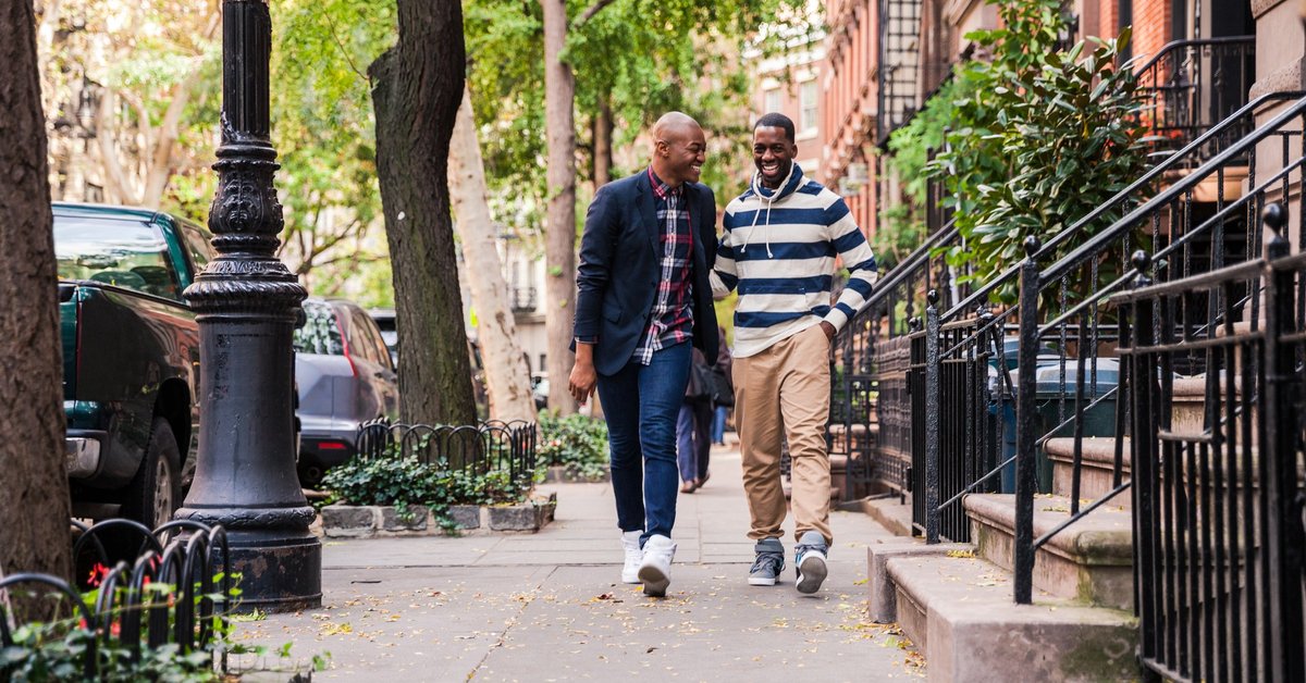 Two men laughing while walking down a residential city street.
