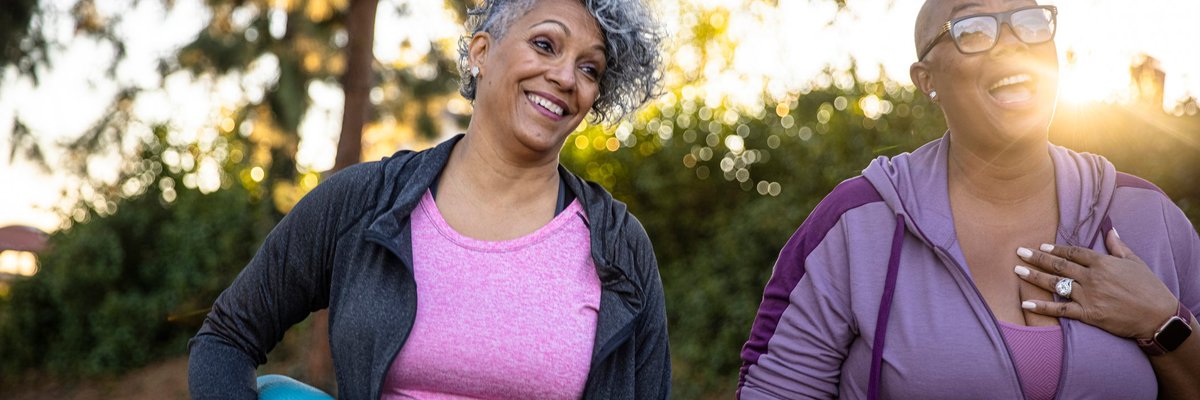 Two smiling middle age adults outdoors with yoga mats.