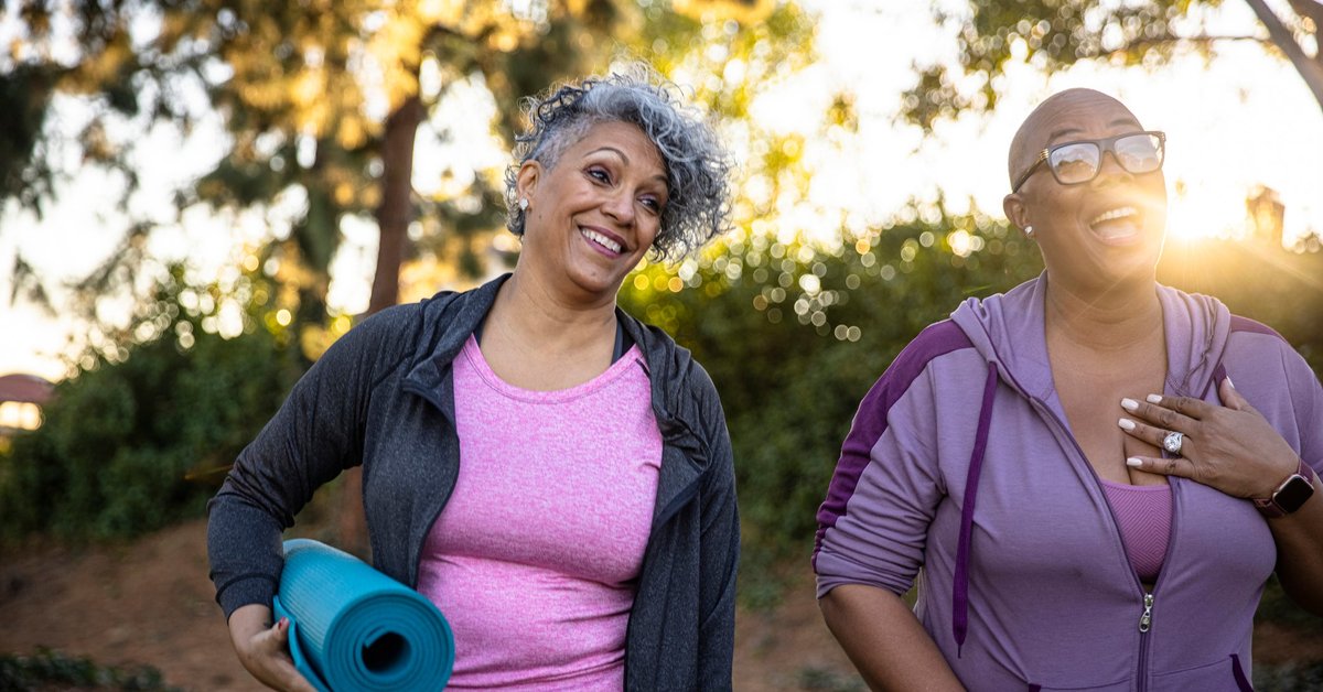 Two smiling middle age adults outdoors with yoga mats.