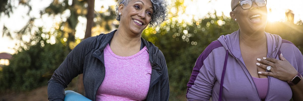 Two smiling middle age adults outdoors with yoga mats.