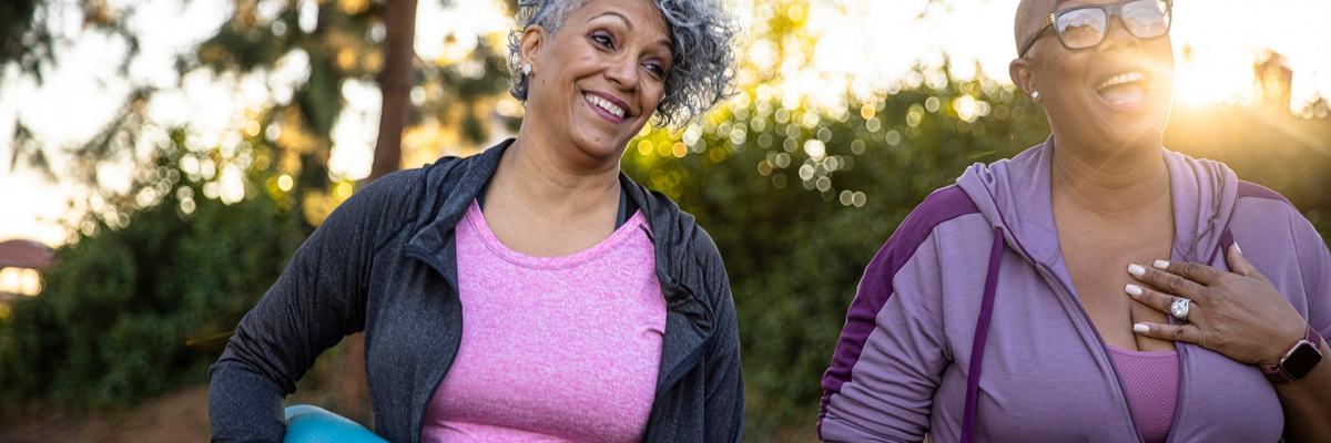 Two smiling middle age adults outdoors with yoga mats.