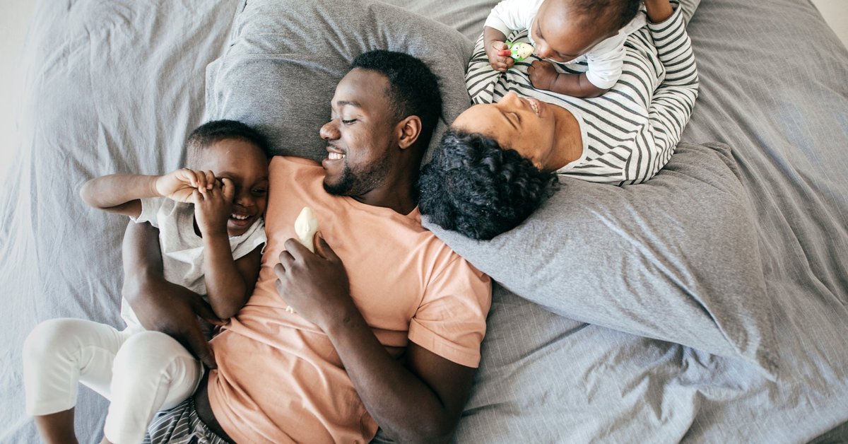 Two parents laying on their bed with their young children.