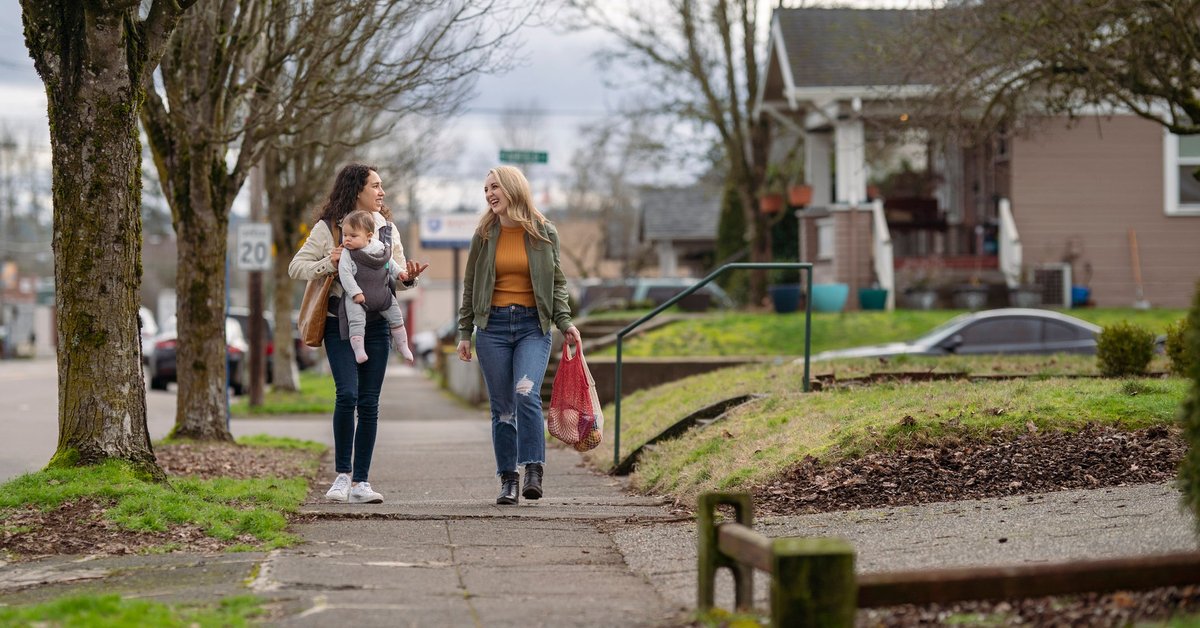 Two people with a baby walking down a residential street and carrying groceries.