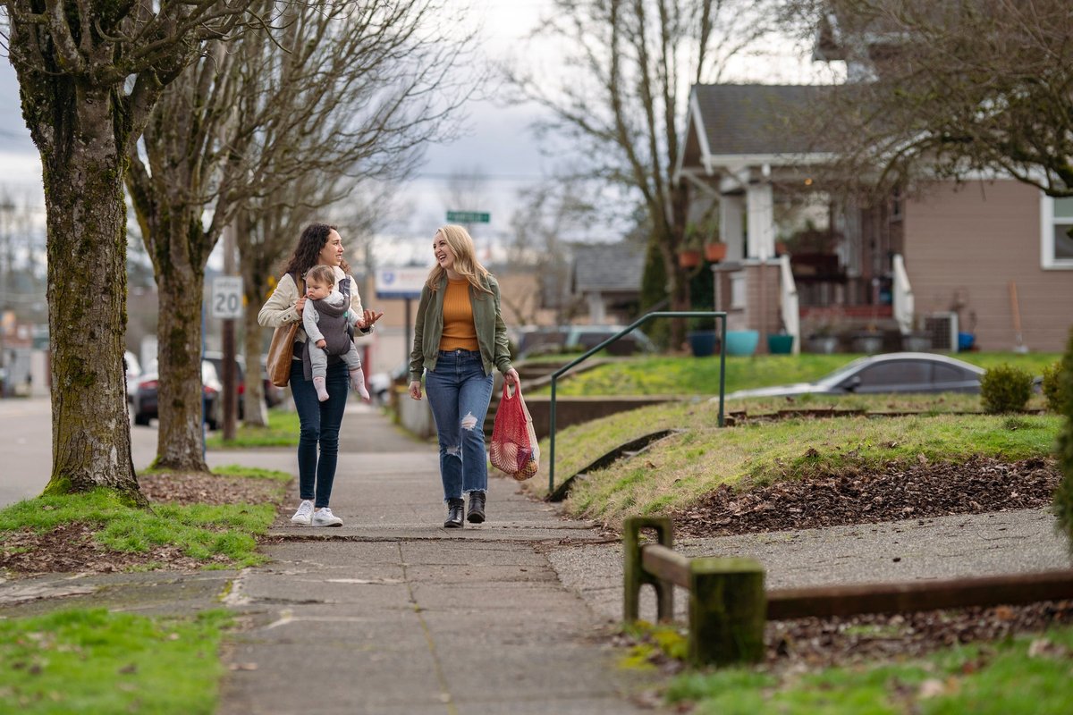 Two people with a baby walking down a residential street and carrying groceries.