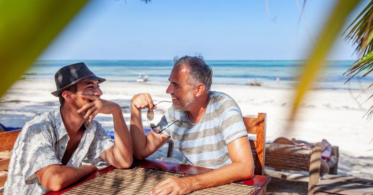 Two smiling people sitting at a table on a tropical beach.