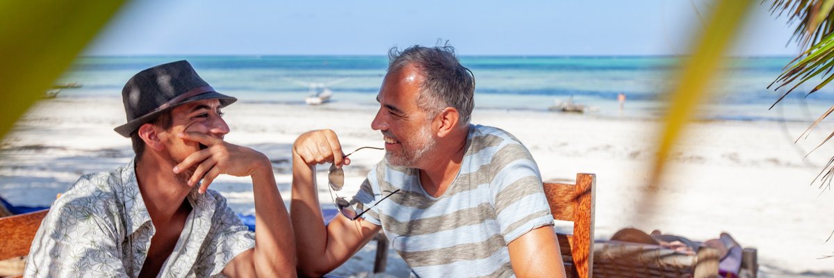 Two smiling people sitting at a table on a tropical beach.