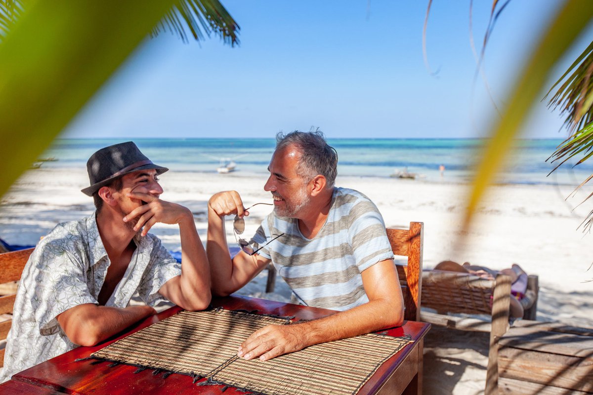 Two smiling people sitting at a table on a tropical beach.