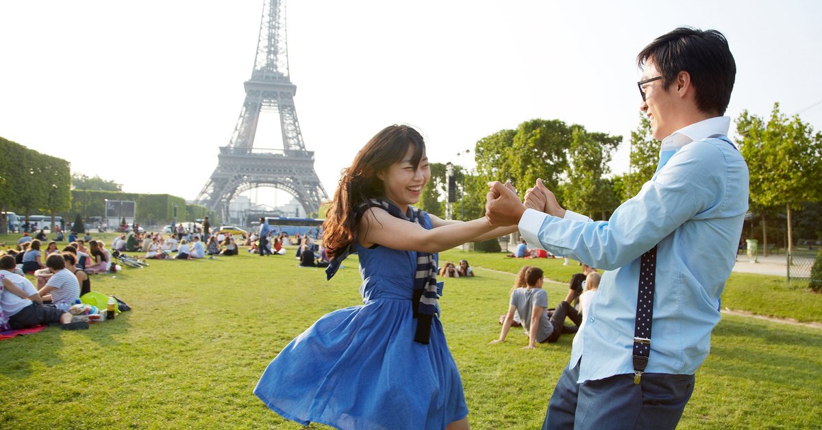 Two smiling people holding hands and standing in the grass in front of the Eiffel Tower in Paris, France.