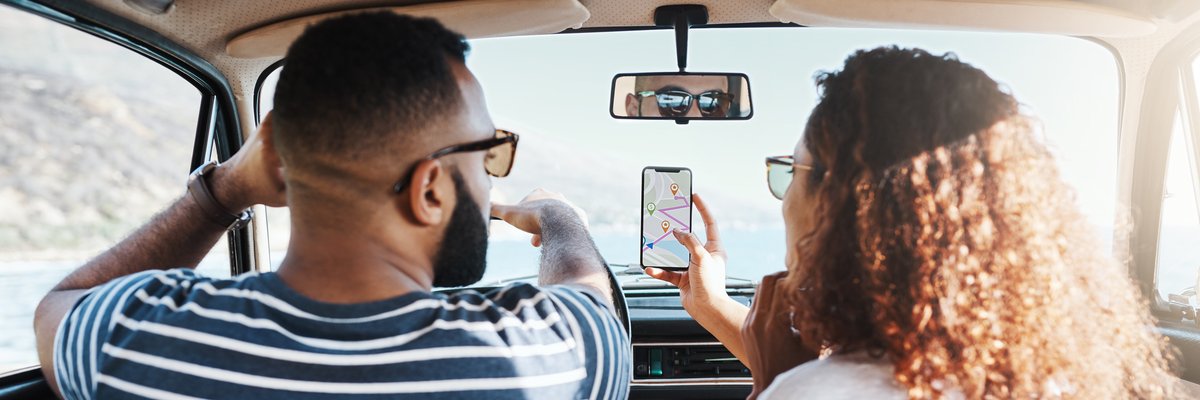 Two people driving in a car on a sunny day while looking up directions on a smartphone.