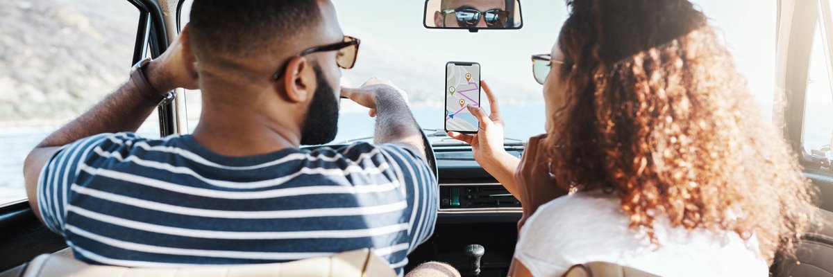 Two people driving in a car on a sunny day while looking up directions on a smartphone.