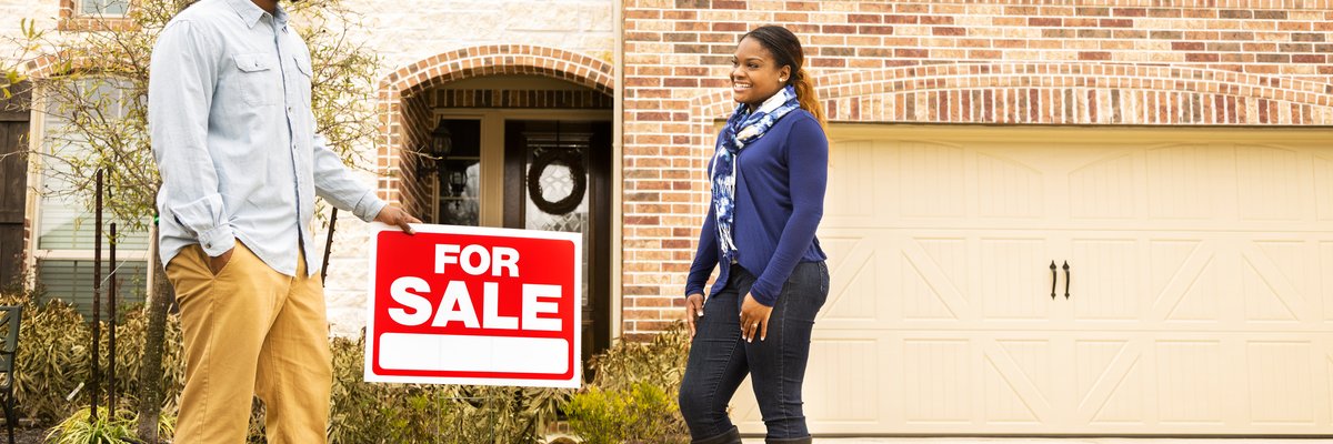 Two people standing next to a For Sale sign in front of a house.