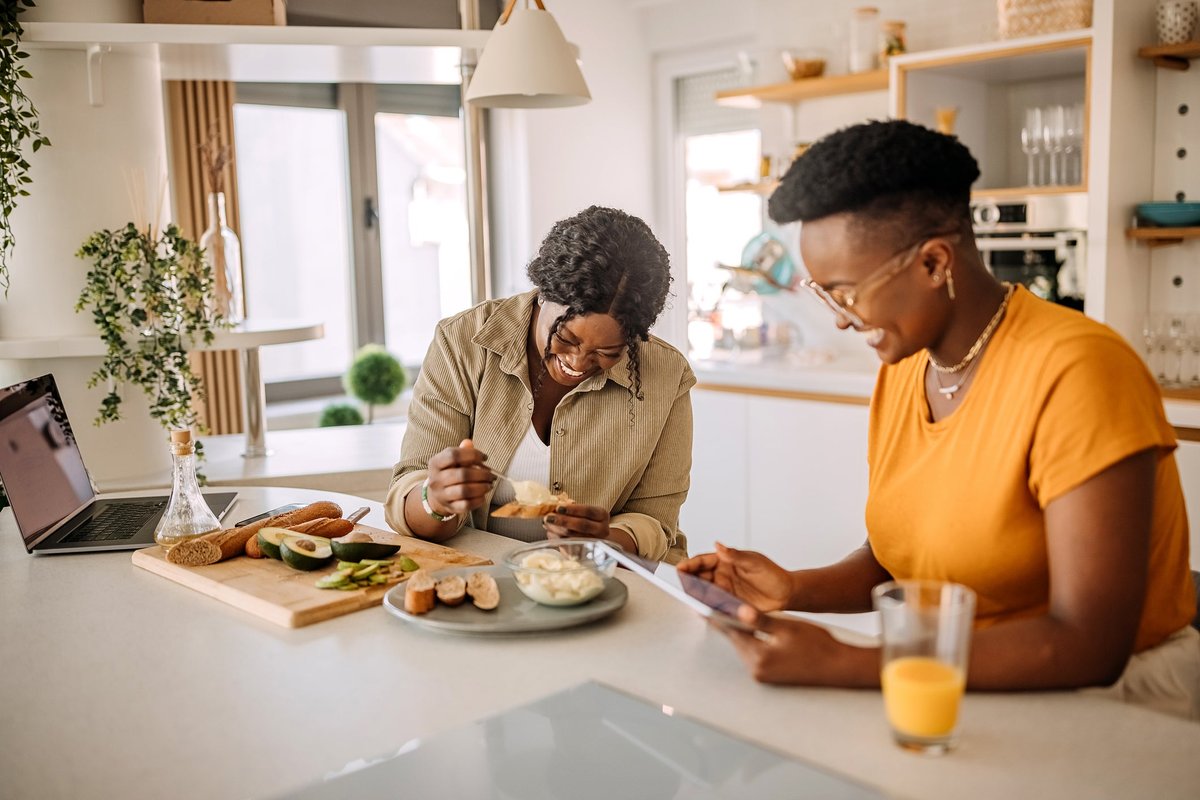 Two people smiling while eating at a kitchen counter.