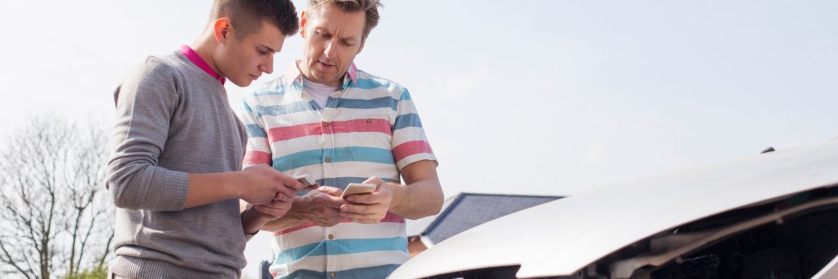 Two people exchanging information with their phones while standing over their cars after a fender bender.