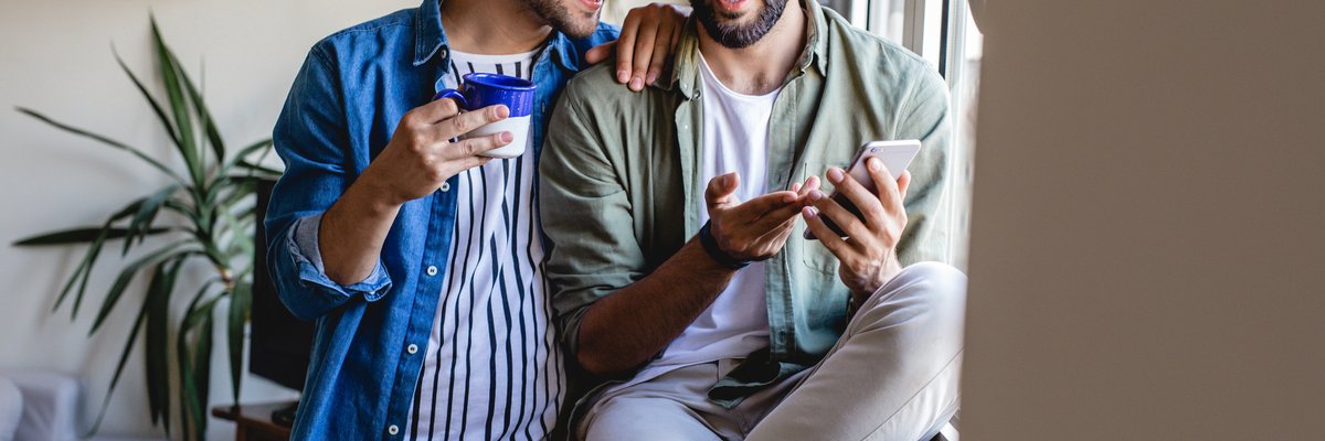 Two people sitting in a window at home and looking at the phone in one of their hands.