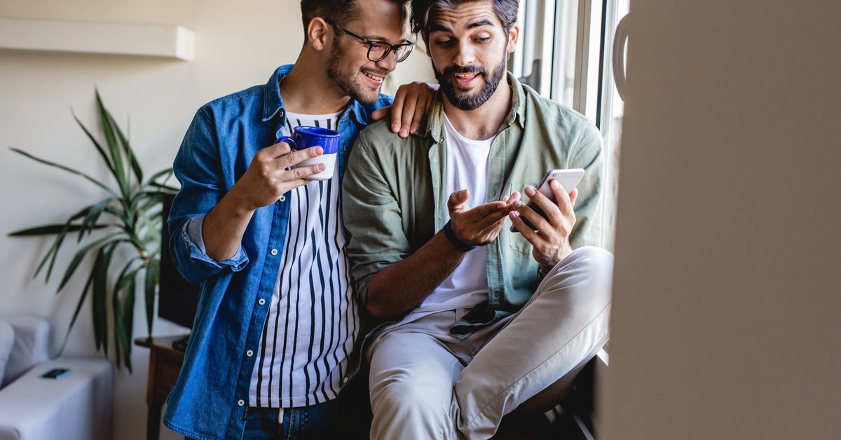 Two people sitting in a window at home and looking at the phone in one of their hands.