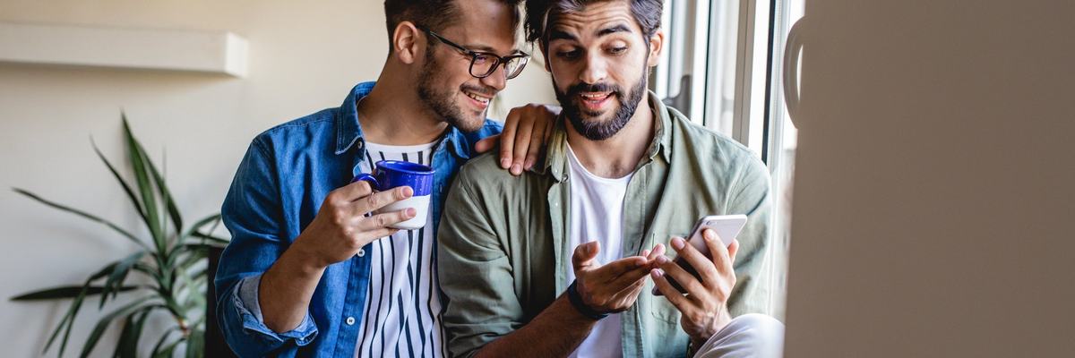 Two people sitting in a window at home and looking at the phone in one of their hands.